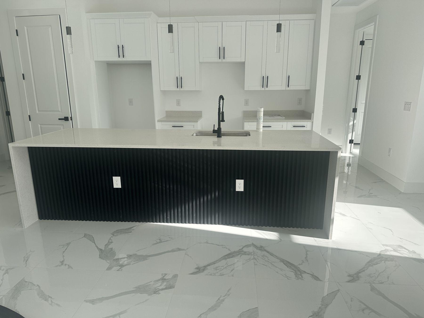 New kitchen with black fluted island, white shaker cabinets and marble-look floors